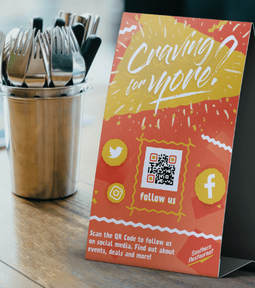 Un display de mesa en un restaurante con un código QR que le lleva a la página para seguir las cuentas de las redes sociales.