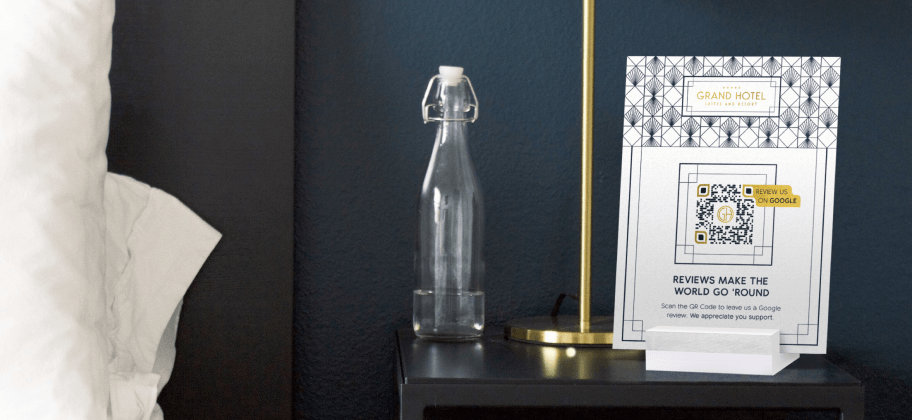 Una mesilla de noche en una habitación de hotel con una botella de agua, una lámpara y una pantalla de mesa con un código QR.